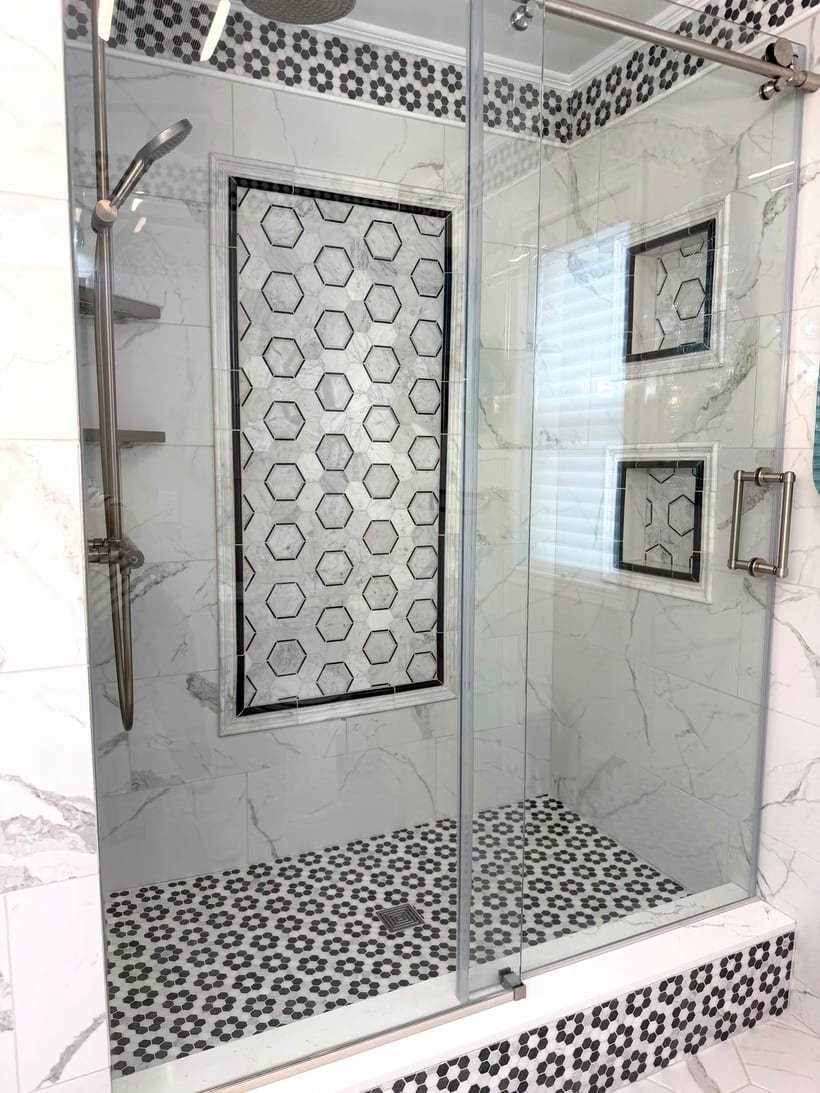Frameless glass tile shower with marble walls, a hexagon mosaic feature wall and built-in niches