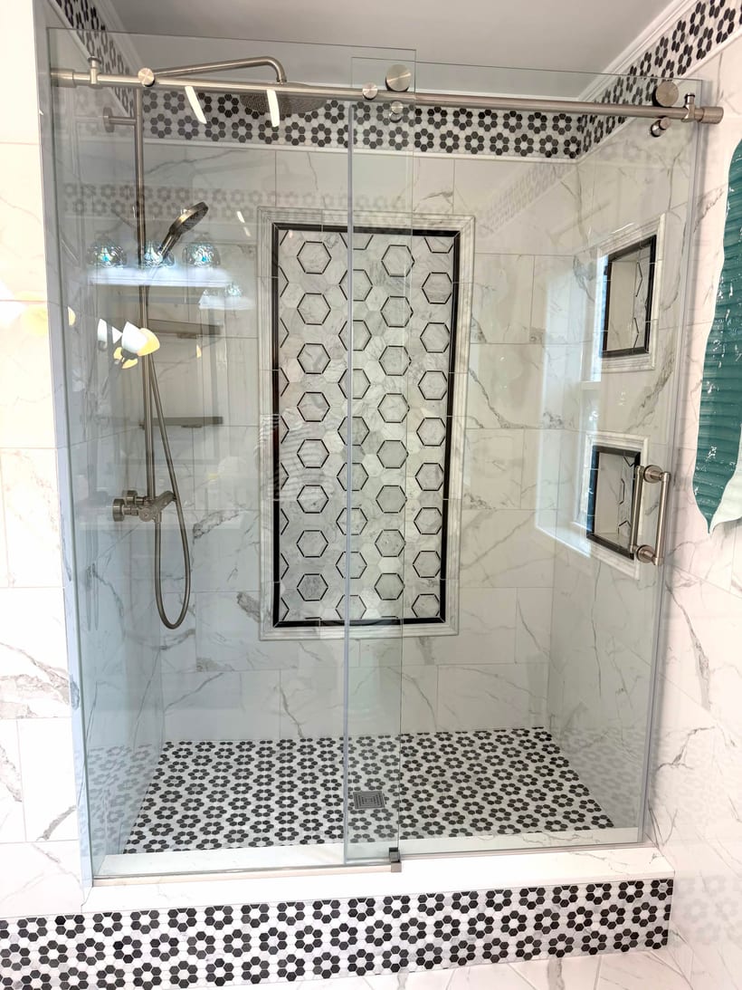 Frameless glass tile shower with marble walls, a hexagon mosaic feature wall and built-in niches