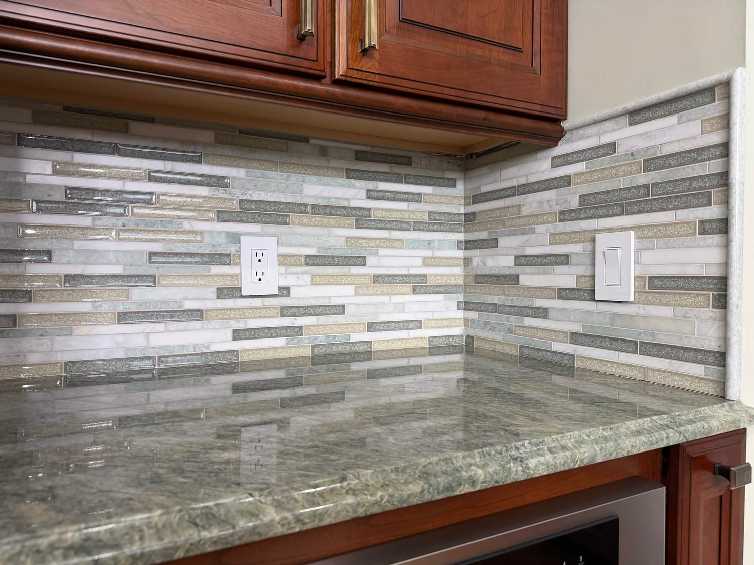 Linear glass and stone mosaic backsplash with granite counter and under cabinet outlet